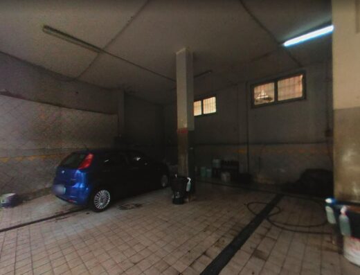 Interno di un autolavaggio a mano con auto blu in attesa di lavaggio, attrezzature per la pulizia e illuminazione industriale.