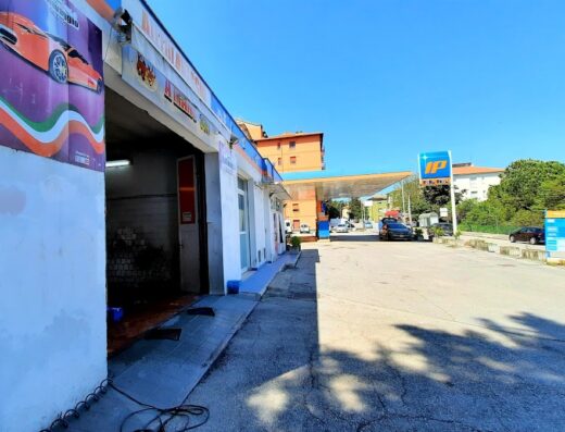 Autolavaggio a mano con insegna colorata e ingresso visibile, situato vicino a una stazione di servizio IP. Servizio professionale per la cura e pulizia del tuo veicolo.