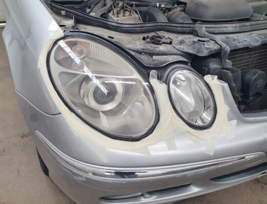 Autolavaggio a Mano Alfons Gressan: Dettaglio del faro di un'auto grigia, preparato con nastro adesivo per la pulizia e la lucidatura professionale.