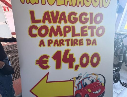 Cartello pubblicitario di Autolavaggio a mano Cleopatra con l'offerta "Lavaggio completo a partire da 14,00 euro" e l'immagine di un'auto sorridente.