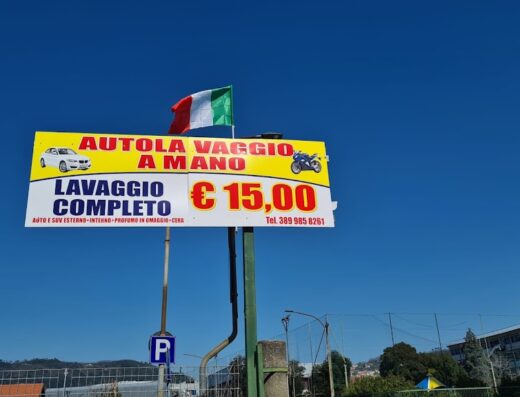 Cartello pubblicitario dell'autolavaggio a mano "Gli Egiziani" al porto, con bandiera italiana, che offre lavaggio completo per auto e moto a 15 euro.