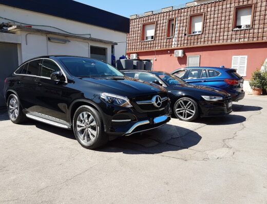 Autolavaggio a mano Hossain: primo piano di una Mercedes nera e altre auto in attesa del servizio di pulizia e cura auto.