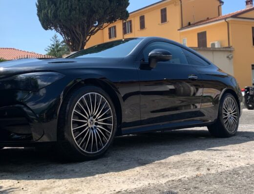 Primo piano di una Mercedes nera appena lavata presso Autolavaggio A mano LE PRESTIGE, con una moto sullo sfondo.