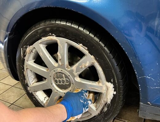 Dettaglio di un autolavaggio a mano MULTISERVICE S.R.L. con la pulizia accurata dei cerchi in lega di un'auto blu.
