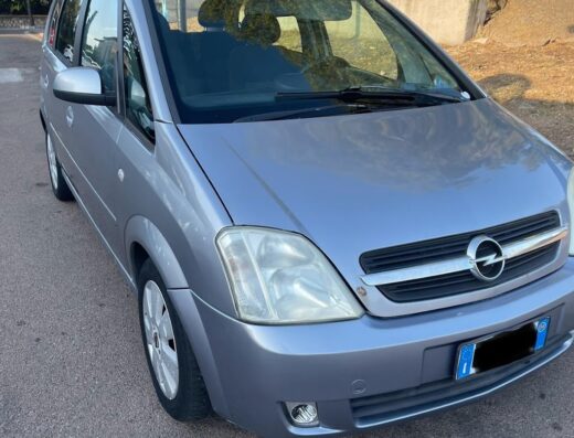 Autovettura Opel Meriva grigia con portellone posteriore aperto, parcheggiata su strada asfaltata, ideale per autolavaggio Alex.