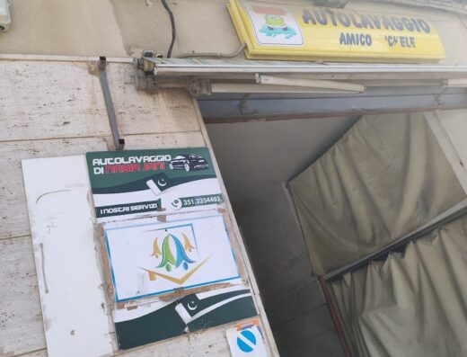 Insegna dell'Autolavaggio Amico Michele con cartelli che indicano i servizi offerti, tra cui lavaggio auto di Nasir Jani, e un numero di telefono.