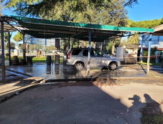 Un'auto grigia in un autolavaggio self-service Apuano, con attrezzature per la pulizia e gettoni. Servizi di lavaggio auto per viaggiatori e motociclisti.