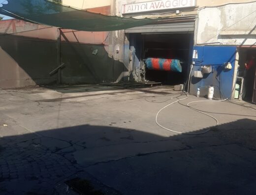 Autolavaggio Basso Acquar: Esterno di un autolavaggio con insegna "AUTOLAVAGGIO", saracinesca abbassata e spazzole di lavaggio visibili all'interno.