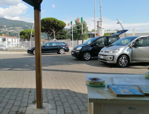 Autolavaggio Brillante: vista di auto in attesa di lavaggio, con bandiere italiane e sfondo montano in una giornata soleggiata.