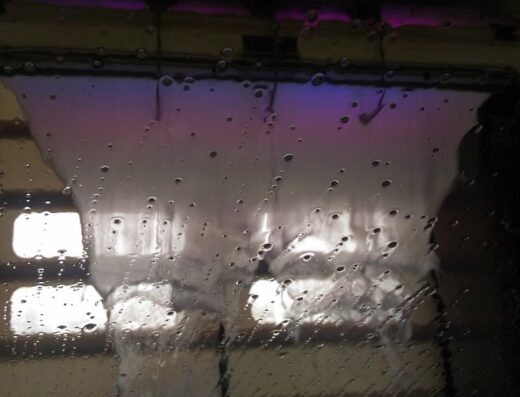 Interno di un autolavaggio Brilli durante il ciclo di lavaggio, con acqua e schiuma che scorrono sul parabrezza.