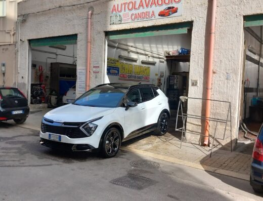 Autolavaggio Candela: A white Kia Sportage SUV parked outside the car wash entrance, with other vehicles visible in the background.