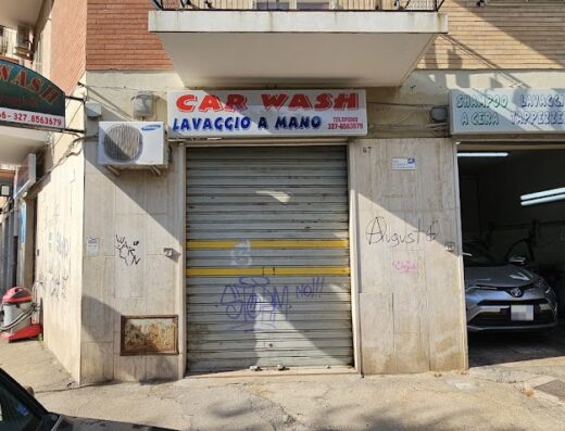 Autolavaggio "Car Wash" a mano con saracinesca abbassata e insegne pubblicitarie. Servizi di shampoo, lavaggio a cera, tappezzeria e motore per moto e auto.
