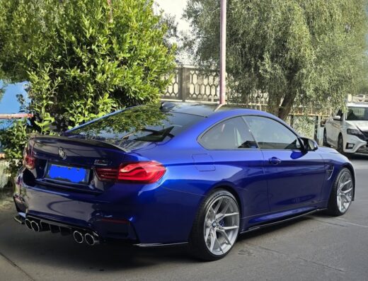 Dettaglio posteriore di una BMW blu metallizzato in un autolavaggio, con scarichi cromati e cerchi in lega. Servizi di pulizia auto.