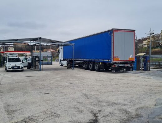 Autolavaggio Clean Car: Un grande camion con rimorchio blu è in attesa per il lavaggio auto self-service, con altre auto in fila.