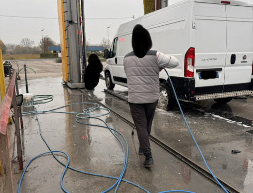 Autolavaggio Colautti: Furgone bianco in fase di lavaggio automatico, operatore con idropulitrice, accessori come tubi a terra.