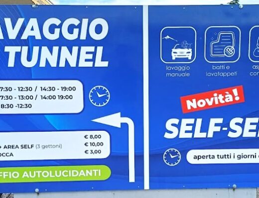 Cartello pubblicitario dell'Autolavaggio De Togni Agostino, che offre servizi di lavaggio a tunnel servito con personale e area self-service. Indicati orari, prezzi e servizi come lavaggio manuale, aspirazione e pulizia interni.