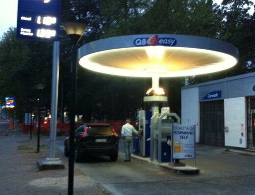 Un uomo fa rifornimento di carburante presso una stazione di servizio Q8 Easy con servizio di autolavaggio, con auto parcheggiata.