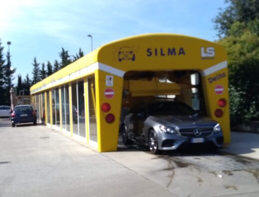 Autolavaggio di Razgui Mohsen: un'auto grigia in un autolavaggio giallo e bianco, con il marchio SILMA LS, per la pulizia e la manutenzione del veicolo.