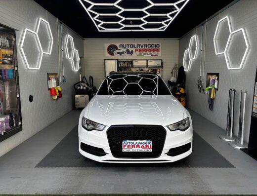 Un'Audi bianca in un autolavaggio Ferrari, con illuminazione esagonale a LED e attrezzature per la pulizia professionale visibili.