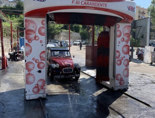 Autolavaggio Fratelli Carandente S.R.L.: Una Citroen 2CV rossa sta per entrare in un autolavaggio automatico con spazzole rotanti, servizio di pulizia auto.