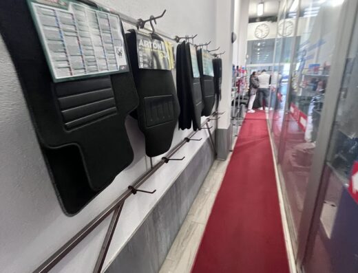 Esposizione di tappetini auto Airton presso Autolavaggio Furiati, con corridoio rosso e clienti sullo sfondo