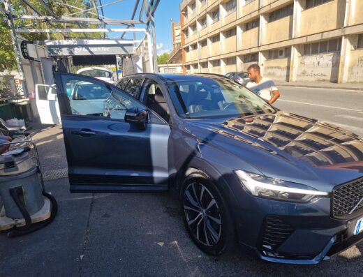 Autolavaggio a Genova: Volvo scura con portiera aperta durante il lavaggio auto self-service con operatore sullo sfondo.