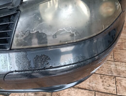 Faro anteriore di un'auto nera che mostra segni di usura e opacizzazione, necessita di un servizio di autolavaggio Il Principe per la pulizia e il ripristino.