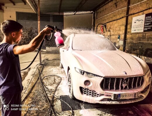Un uomo lava un'auto bianca con una lancia schiumogena presso Autolavaggio Incardona, servizio di car detailing per la cura dell'auto.