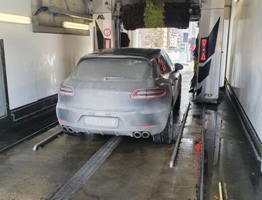 Autolavaggio LUPO 24/7: Una Porsche Macan grigia sporca è all'interno dell'autolavaggio automatico, con le spazzole pronte a pulirla.