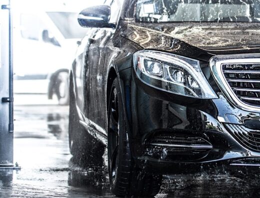Primo piano di una Mercedes nera in un autolavaggio a Mestre, con acqua che scorre sulla carrozzeria e sui fari