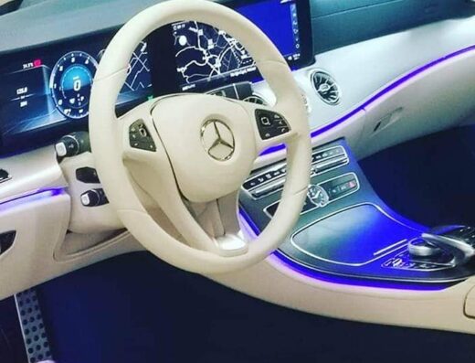 Interni lussuosi di un'auto Mercedes-Benz con volante bianco e illuminazione blu, dettaglio del cruscotto e del sistema di navigazione.