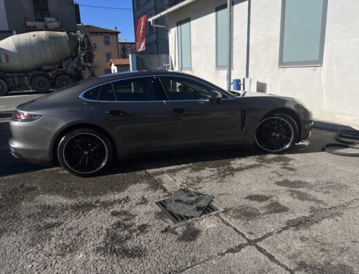 Autolavaggio Oasi Dell'auto: Elegante Porsche Panamera grigia appena lavata con cerchi neri presso l'autolavaggio, sullo sfondo una betoniera.