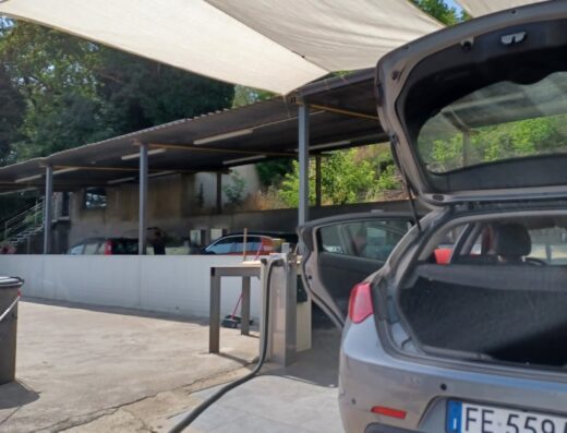 Autolavaggio Pastore: Auto grigia con bagagliaio aperto, dettaglio della targa FE 559A, in un'area di lavaggio auto all'aperto con tettoia.