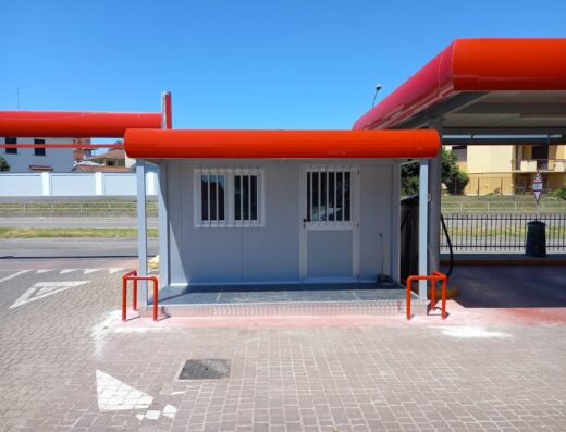 Autolavaggio Pesenti: Cabina esterna grigia con tettoia rossa e barre di protezione rosse, parte del servizio di autolavaggio.