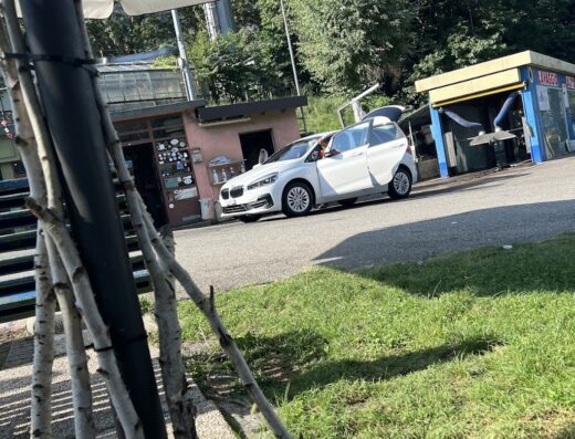 Autolavaggio Rapido: A white BMW hatchback car parked at a car wash station, with the trunk open, ready for a quick and efficient car cleaning service.