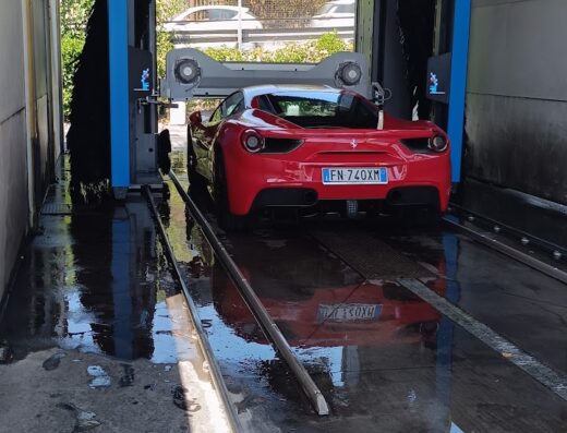 Autolavaggio Relax Car Washing: Una Ferrari rossa in un autolavaggio automatico, dettaglio del retro con la targa "FN 740XM", servizio di pulizia auto.