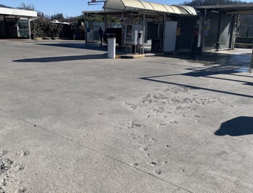 Autolavaggio self-service all'aperto con stalli per il lavaggio moto, attrezzature per la pulizia e ampio piazzale in una giornata di sole.