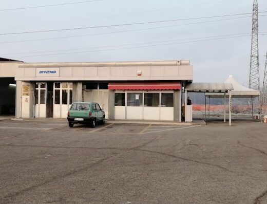 Autolavaggio senza spazzole: edificio con insegna "officina", una macchina verde parcheggiata di fronte e un'area di lavaggio auto.