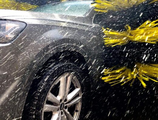 Autolavaggio Silva Assistauto: Close-up of a gray Audi SUV being washed in an automatic car wash with yellow brushes and water spraying.