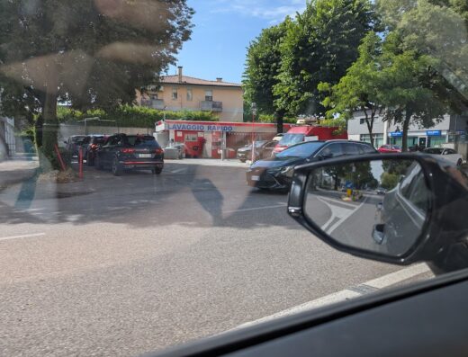 Autolavaggio Simionato: fila di auto in attesa al lavaggio rapido, vista dalla strada con riflesso nello specchietto retrovisore.