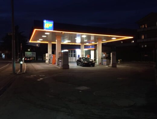 Autolavaggio Speed: stazione di servizio IP illuminata di notte con auto nera sotto la tettoia, distributori visibili.