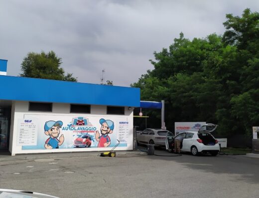 Autolavaggio via Castelleone: A self-service car wash station with two cars being cleaned, featuring a blue and white building with "Autolavaggio" signage and cartoon mascots. Services available for cars and motorcycles.