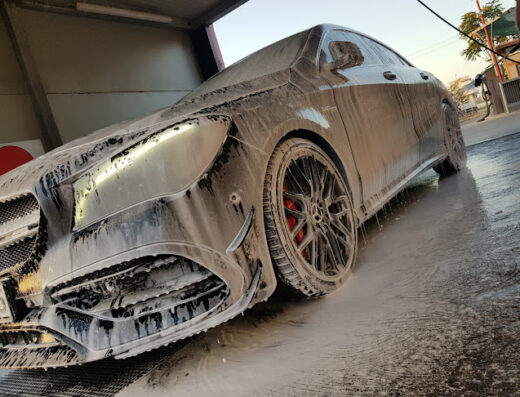 Autolavaggio via Trani: Dettaglio di un'auto nera ricoperta di schiuma durante il lavaggio, con attenzione ai cerchi in lega e ai freni rossi.