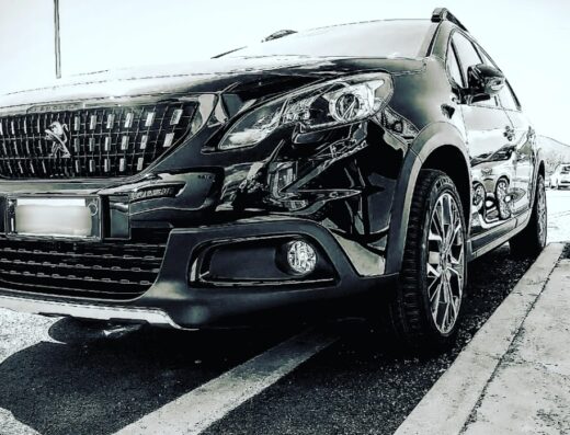 Autolavaggio Zenit: Dettaglio frontale di un'auto nera lucida, probabilmente una Peugeot, parcheggiata su strada. Si notano i dettagli della griglia, dei fari e dei cerchi in lega.