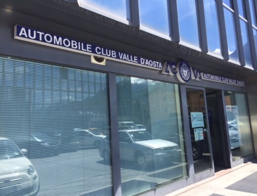 Fotografia della sede dell'Automobile Club Valle d'Aosta, con insegna ben visibile e auto riflesse nelle vetrine.