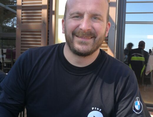 Ritratto di Luca De Piccoli, esperto di automototecnica, con maglietta del suo servizio di riparazione moto personalizzata e logo BMW Motorrad.