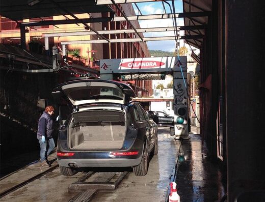 Autolavaggio Calandra: un'auto di colore scuro con il bagagliaio aperto è in fase di lavaggio automatico, operatore in divisa.