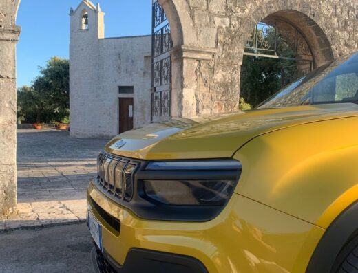Noleggio auto Salento: Dettaglio frontale di una Jeep gialla parcheggiata di fronte ad una chiesa in pietra ad Otranto, Puglia.