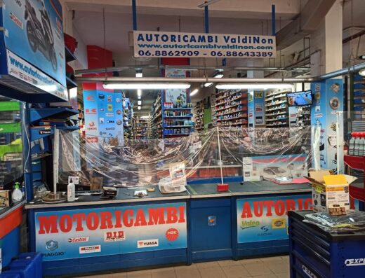 Interno del negozio Autoricambi Val di Non Conca d'Oro, specializzato in ricambi e accessori per moto, con scaffali pieni di prodotti e banco vendita.