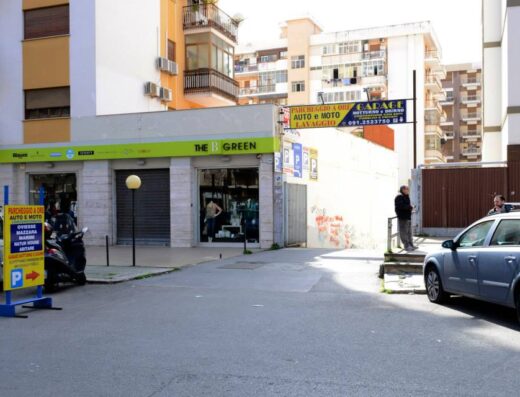 Autorimessa Cannizzaro parcheggio Viale Strasburgo 188 h24: Vista esterna del parcheggio per auto e moto, con insegna "Parcheggio a ore auto e moto" e cartello indicatore con freccia. Visibile anche l'insegna "The B Green" e un'area di lavaggio auto.
